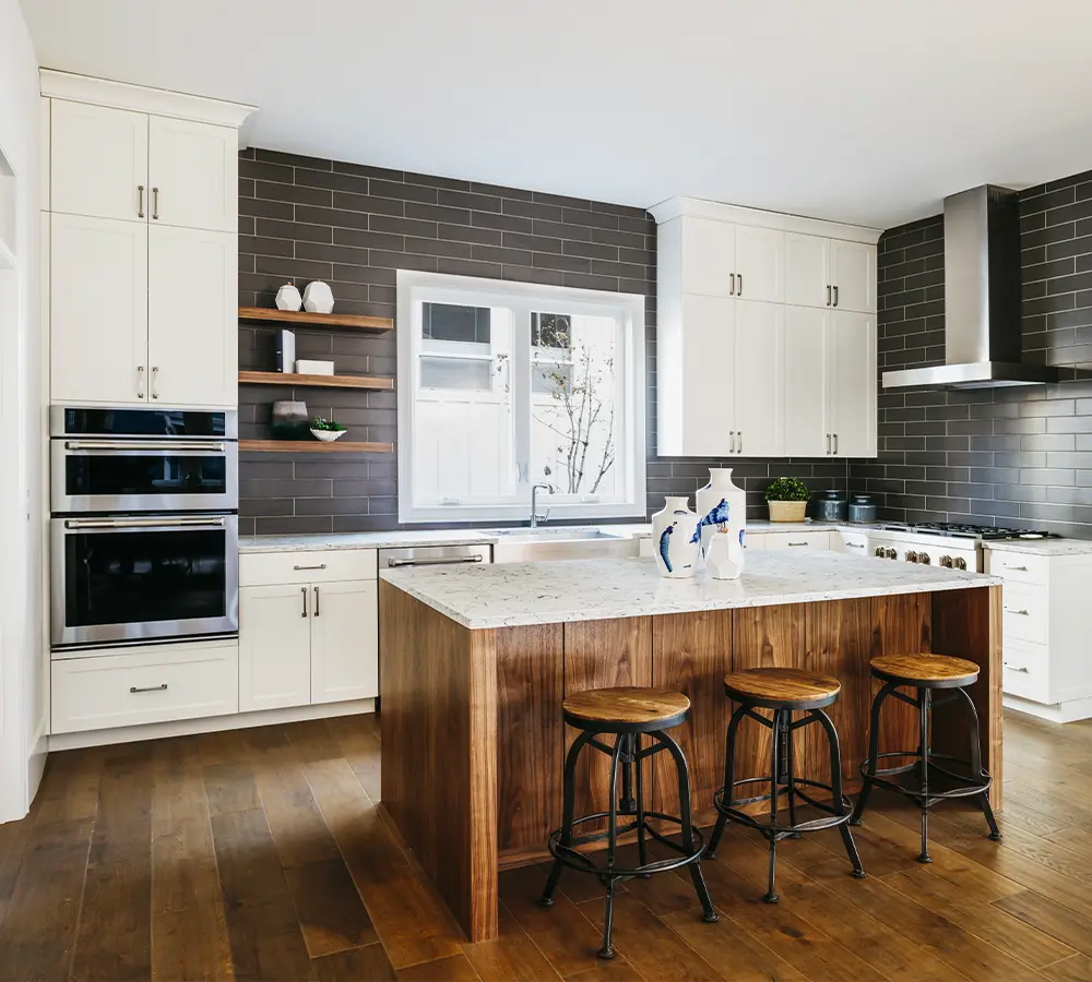 Modern kitchen design featuring a large wooden island with bar stools, white cabinets, and dark subway tile backsplash.