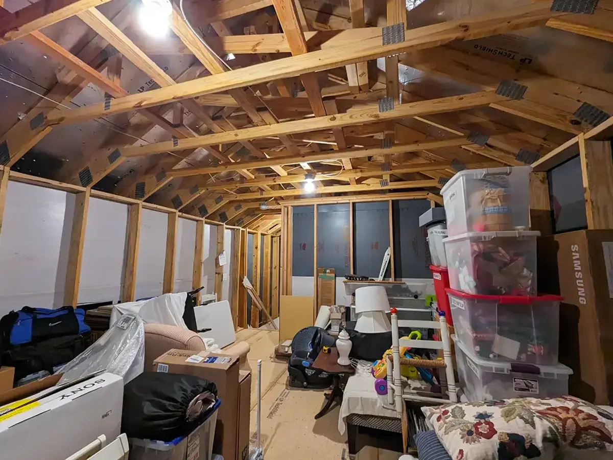 Cluttered attic storage space with wooden beams and exposed insulation before finishing.