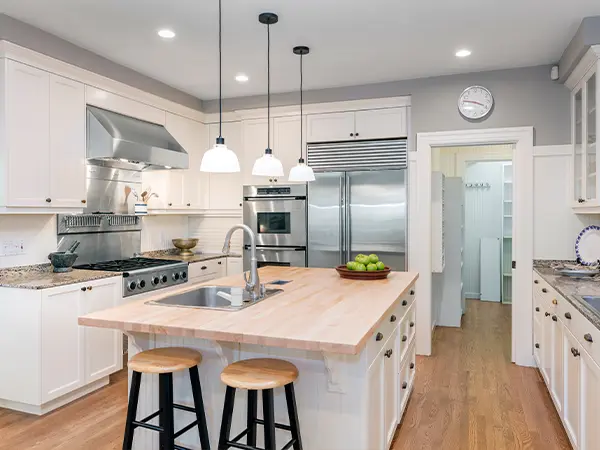 A spacious modern kitchen with white cabinets, wooden flooring, and a central island for cooking and dining.