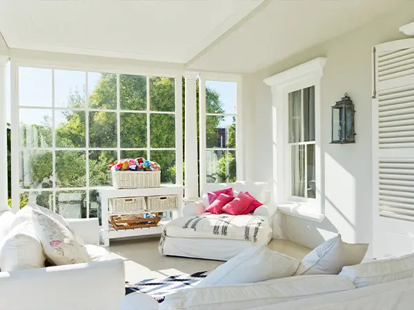 Bright sunroom with panoramic windows, elegant seating, and French doors offering a serene view of lush greenery.