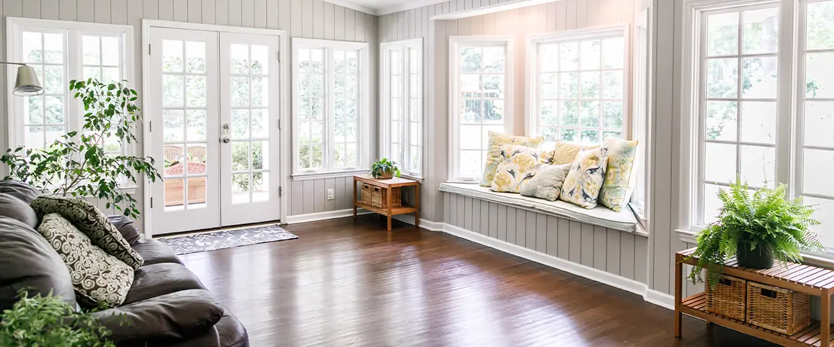 Bright sunroom with large windows, French doors, cozy seating nook, and wooden floor - modern home interior.