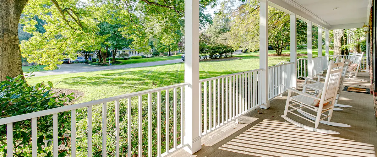 Charming front porch with white railing, rocking chairs, and green lawn view - traditional American porch design.