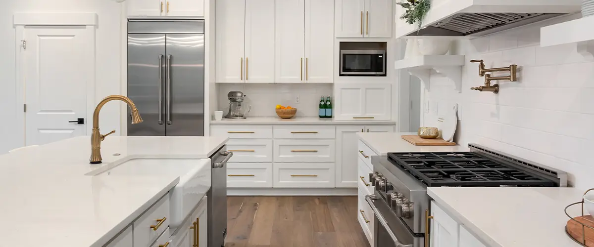 Modern white kitchen with gold accents, featuring stainless steel appliances, white cabinetry, and hardwood floors.