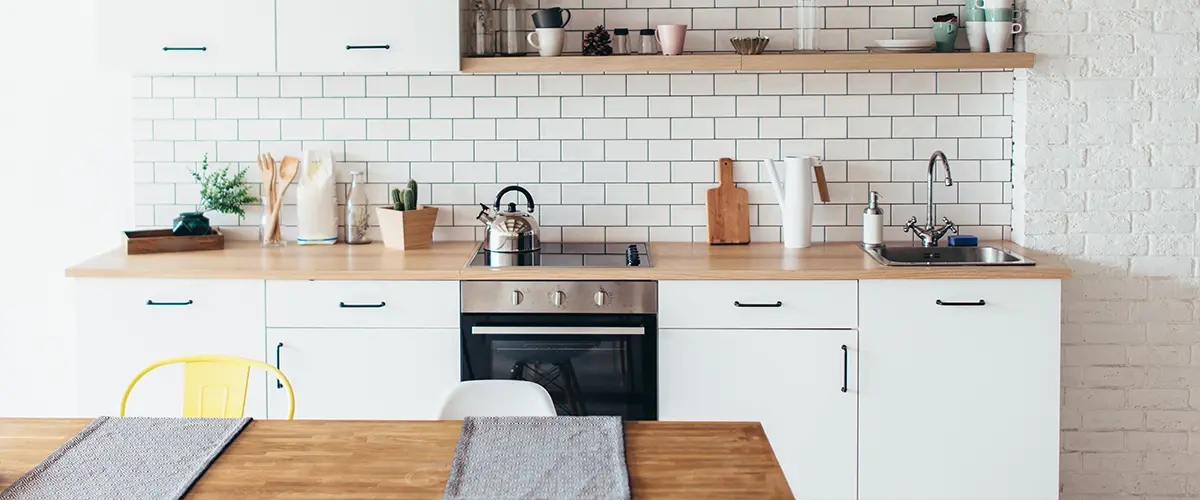 Scandinavian-style minimalist kitchen featuring white cabinetry, subway tile backsplash, and natural wood countertops.