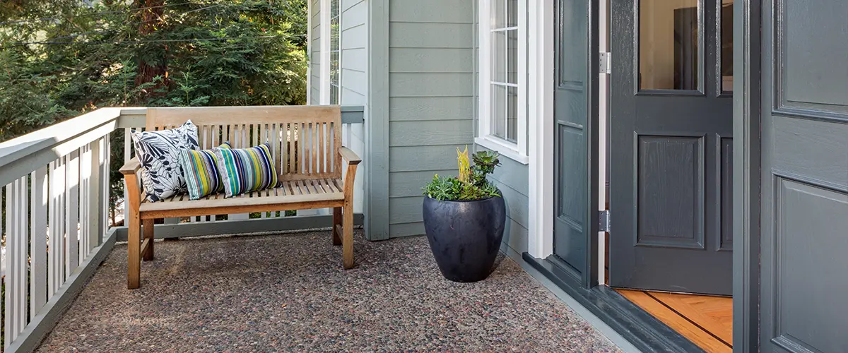 Small balcony with wooden bench, pillows, and green potted plant - cozy outdoor seating area at home entrance.