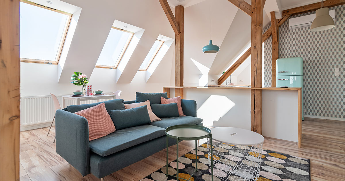 Stylish attic living space featuring exposed wooden beams, vibrant furniture, and abundant natural lighting through skylights.