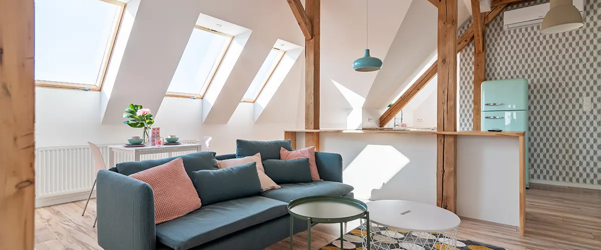 Stylish attic living space featuring exposed wooden beams, vibrant furniture, and abundant natural lighting through skylights.