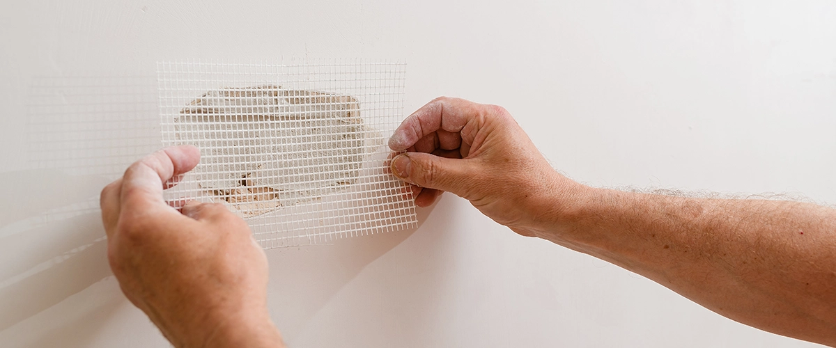 A handyman is repairing a hole in the drywall in the wall