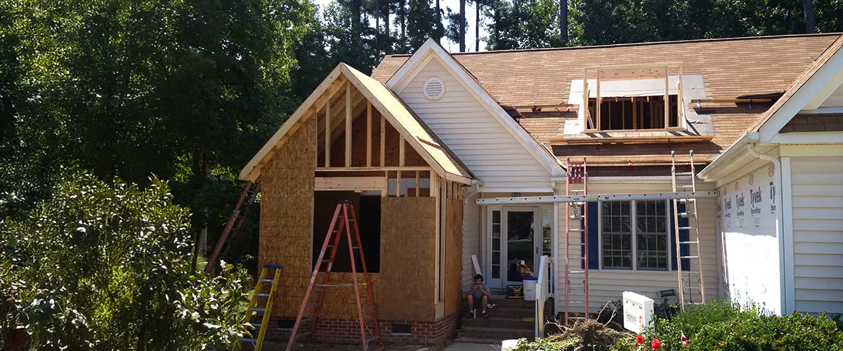 A house undergoing an addition with wooden framing, ladders, and construction materials.